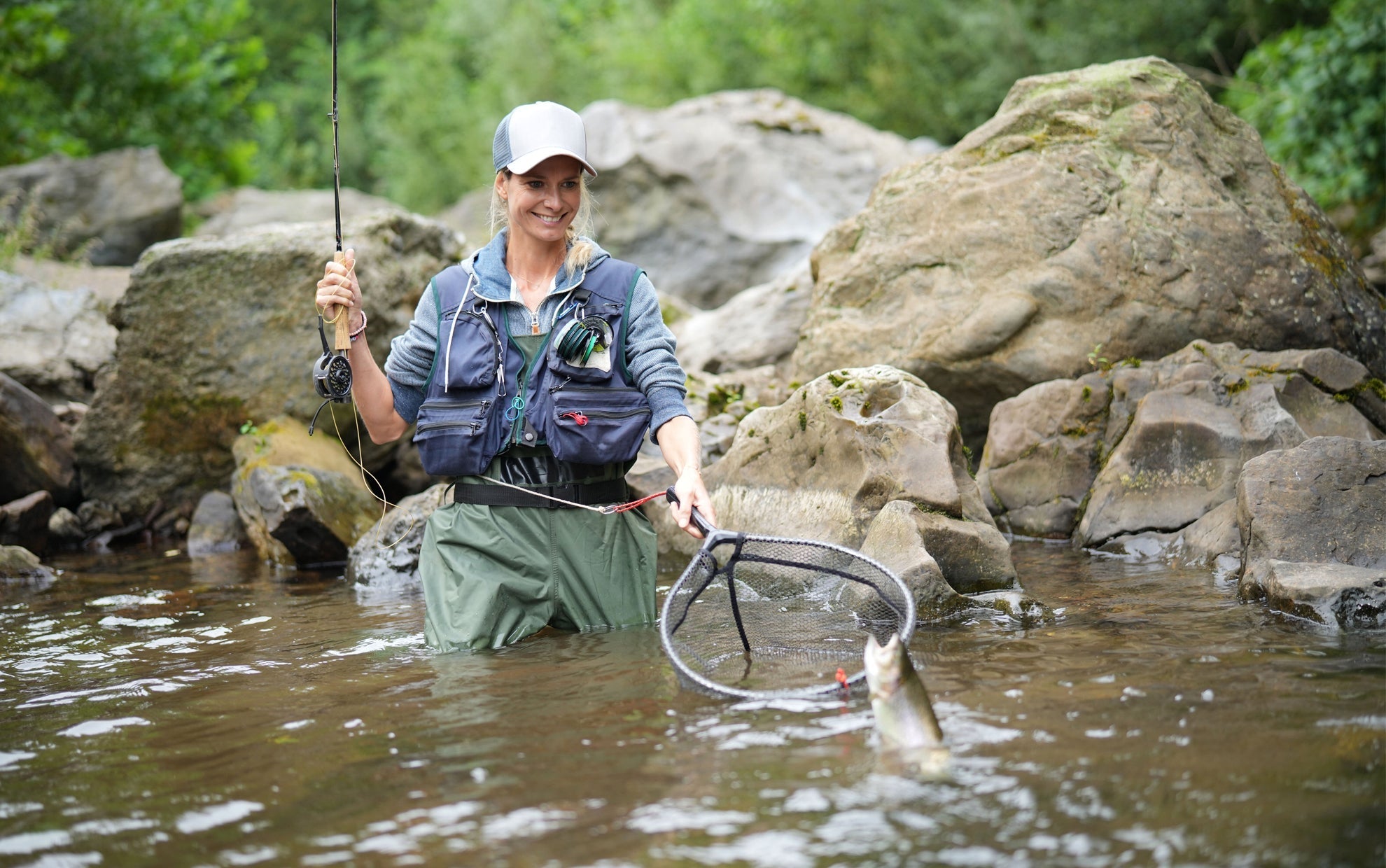 Fly fisher catching trout with Pat's Rubber Legs Nymph in a rocky river setting
